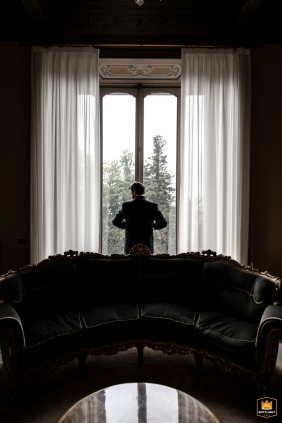 In Varese, Italy, at Villa Montalbano, a formal image captures the groom getting ready by the window, with his reflection visible in the mirror table.